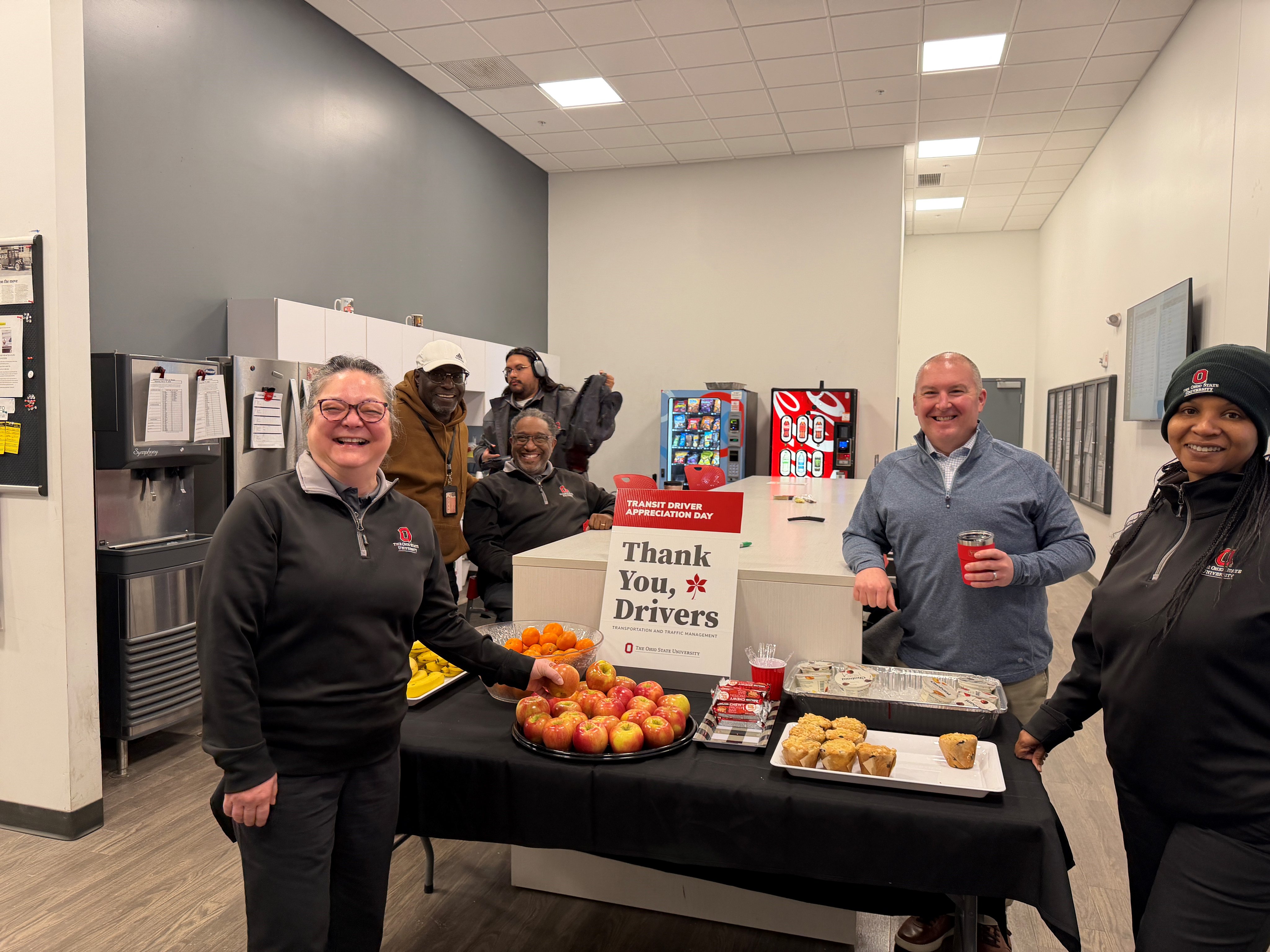 A group of people stand around a table that has snacks on it.