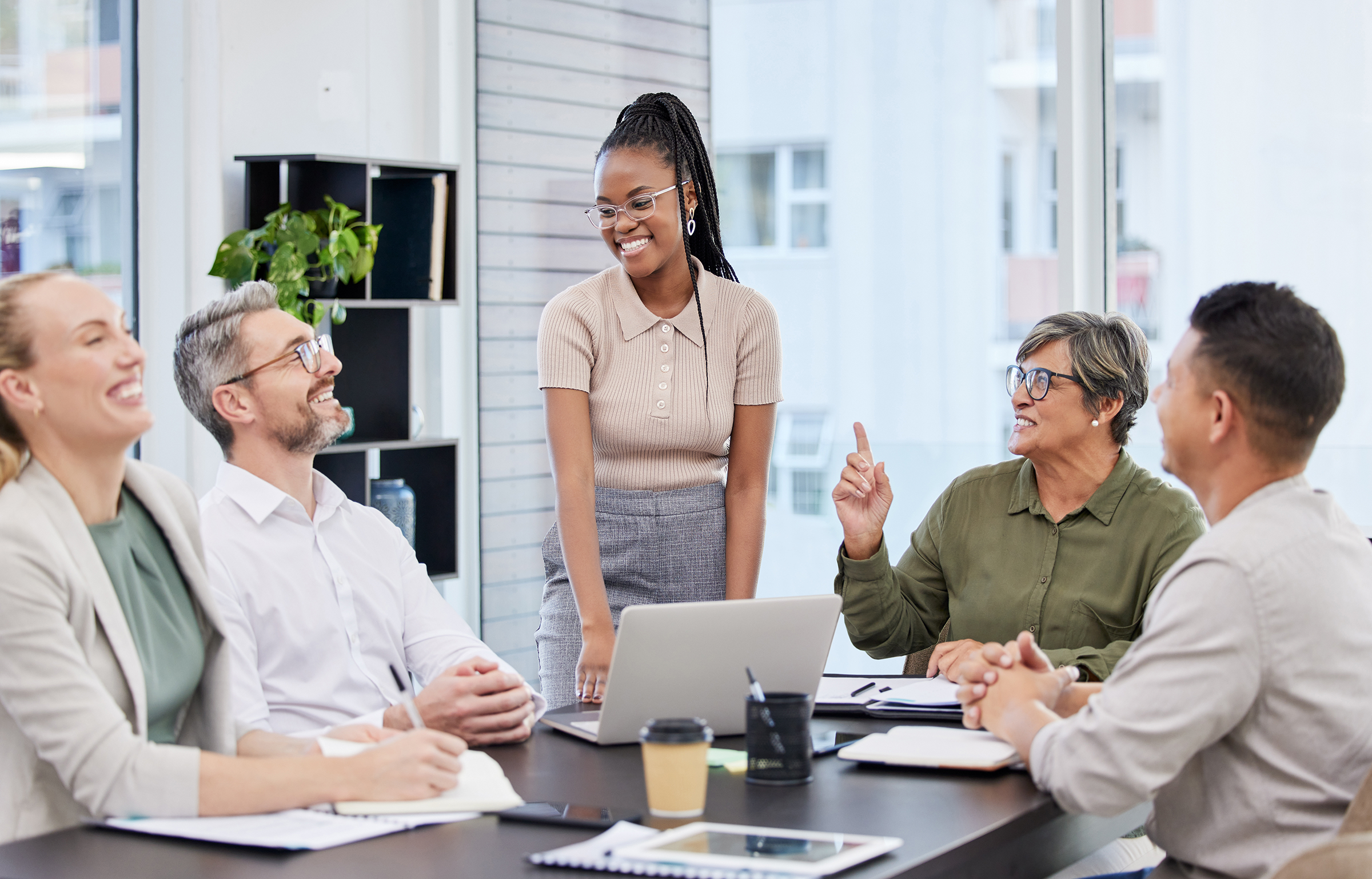 five people talking in an office, sitting and standing around a table