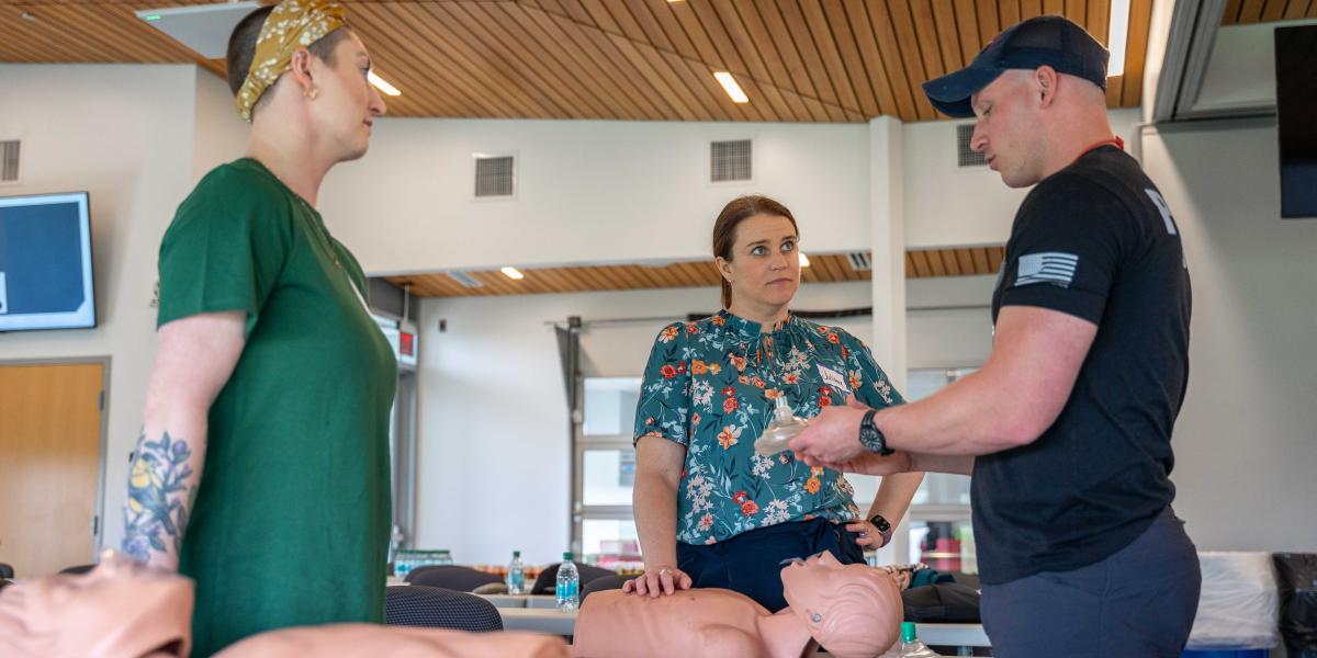 Two women are seen learning how to perform CPR on a mannequin. 