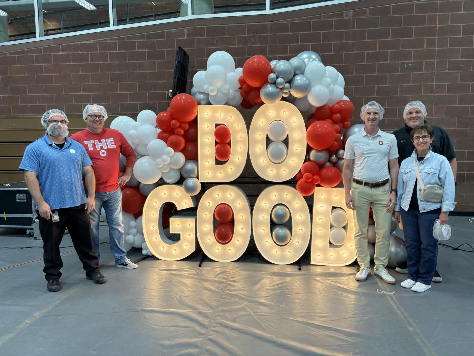 Five people standing on each side of large, lit up letters that spell out, 'DO GOOD'