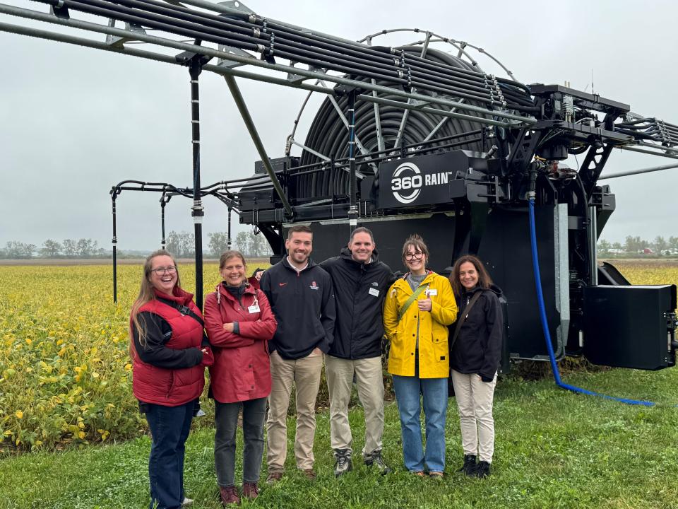 6 people standing outside next to a crop field on a rainy afternoon.